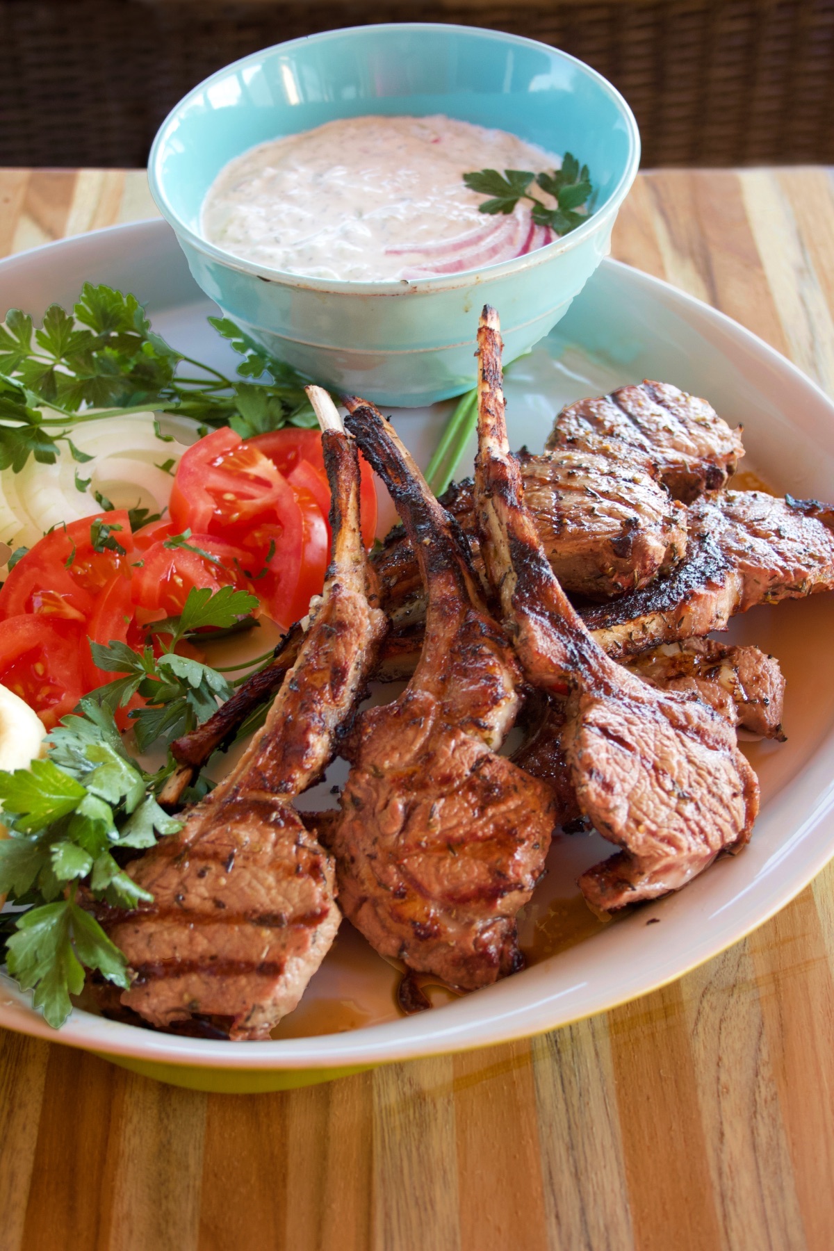 Closeup of the platter of lamb chops, sliced tomato and onion, and tzatziki sauce. 