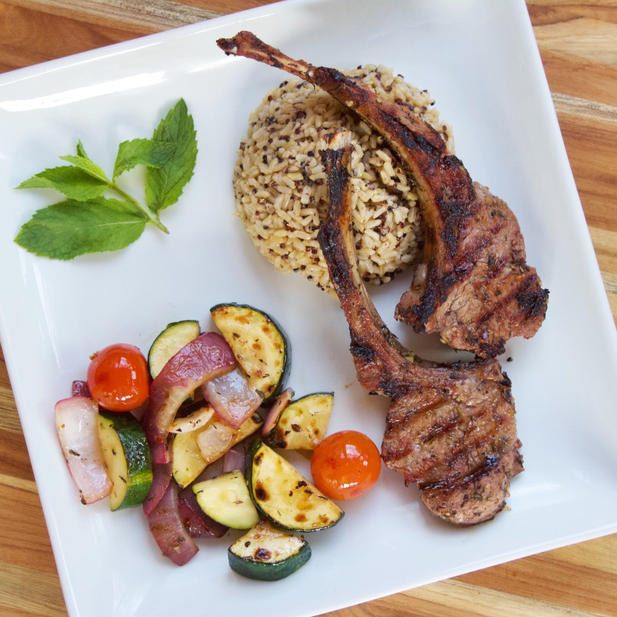 Greek Marinated Lamb Chops served on a white plate with grilled vegetables and a quinoa-brown rice mix.