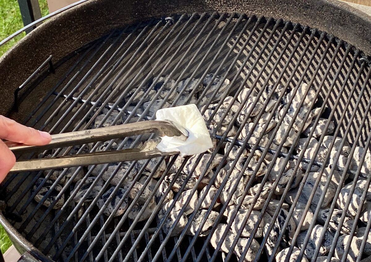 Oiling the cooking grate using a paper towel dipped in vegetable oil, help with a pair of tongs.