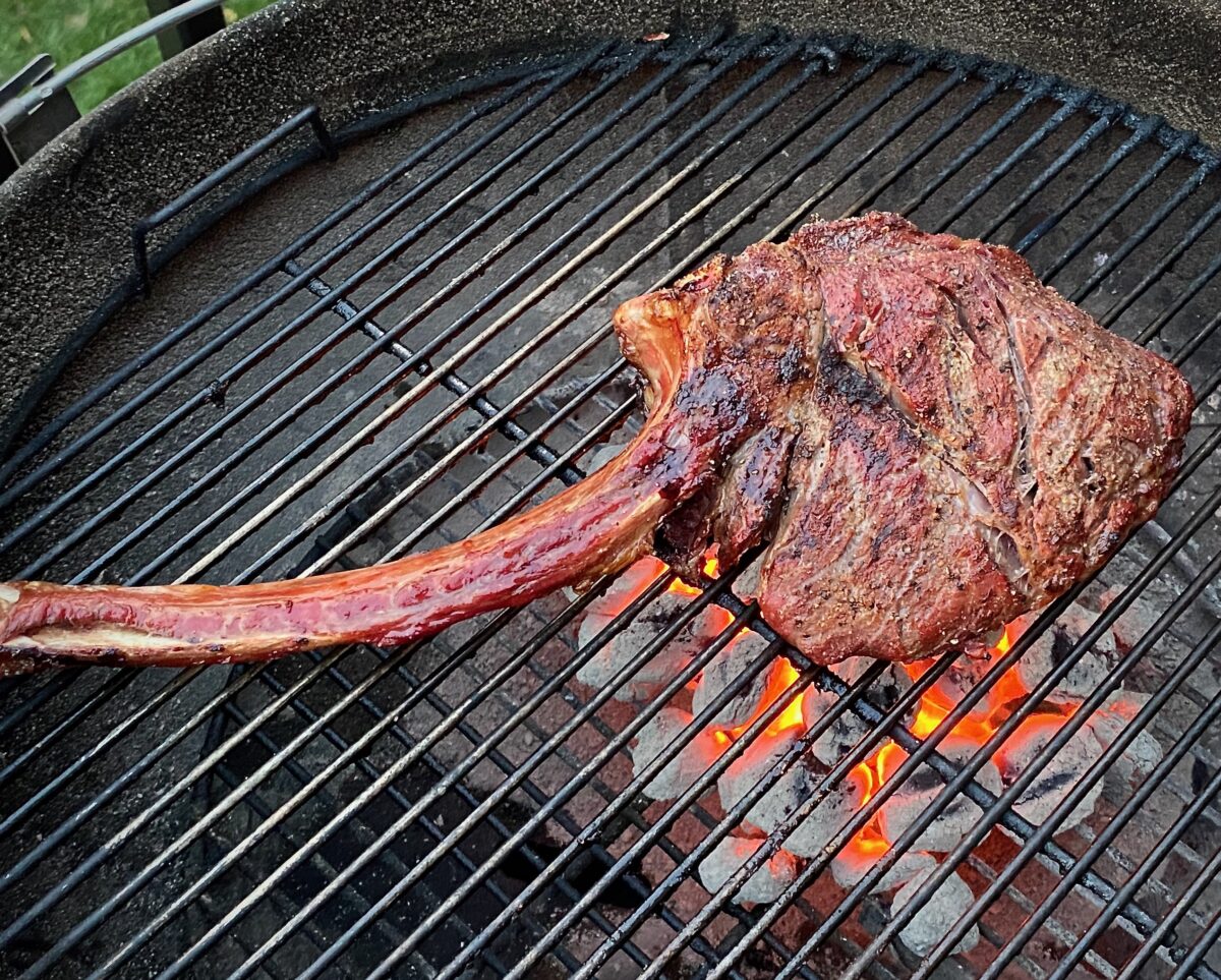 A tomahawk steak on the grill over red-hot colas during the sear phase.