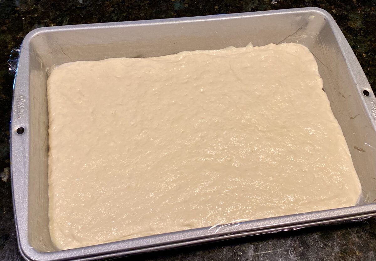 The prepared dough in the plastic wrap-covered pizza pan.
