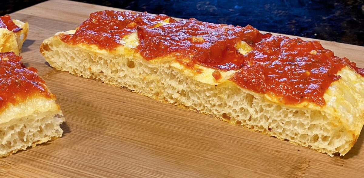 A side view of the sliced pan pizza resting on a cutting board. You can see how light and airy the crust is.