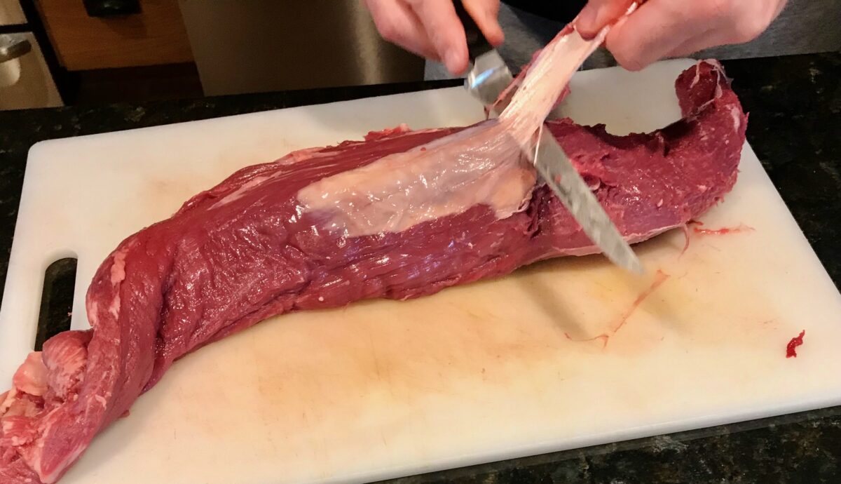 filet knife removing silver skin from whole beef tenderloin.