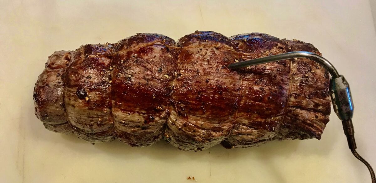 Fully cooked beef tenderloin resting on cutting board.