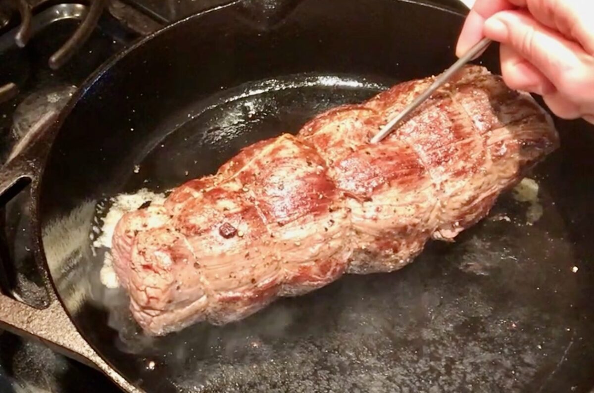 meat thermometer being inserted into beef tenderloin while still in a hot skillet.