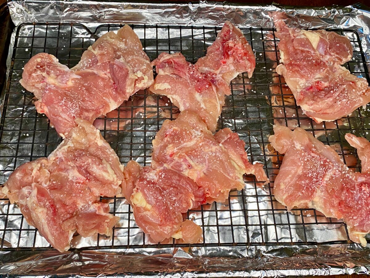Salted chicken thighs on a wire rack set into a foil-lined baking sheet.