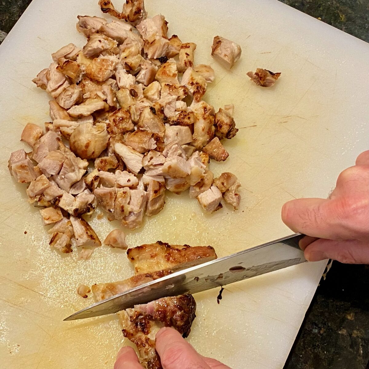 Chopping the rested chicken into bite-size pieces before adding to the sauce.