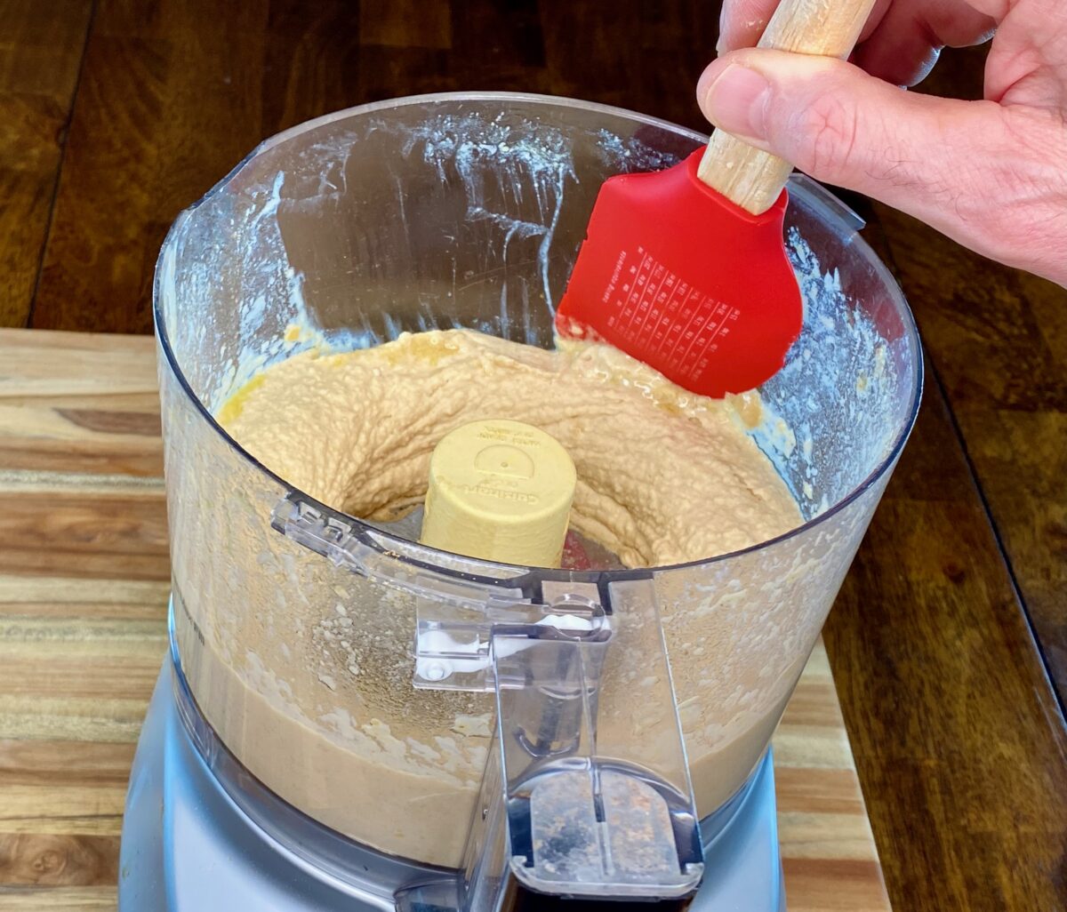Scraping down the sides of the food processor after the hummus has processed for 1 minute.