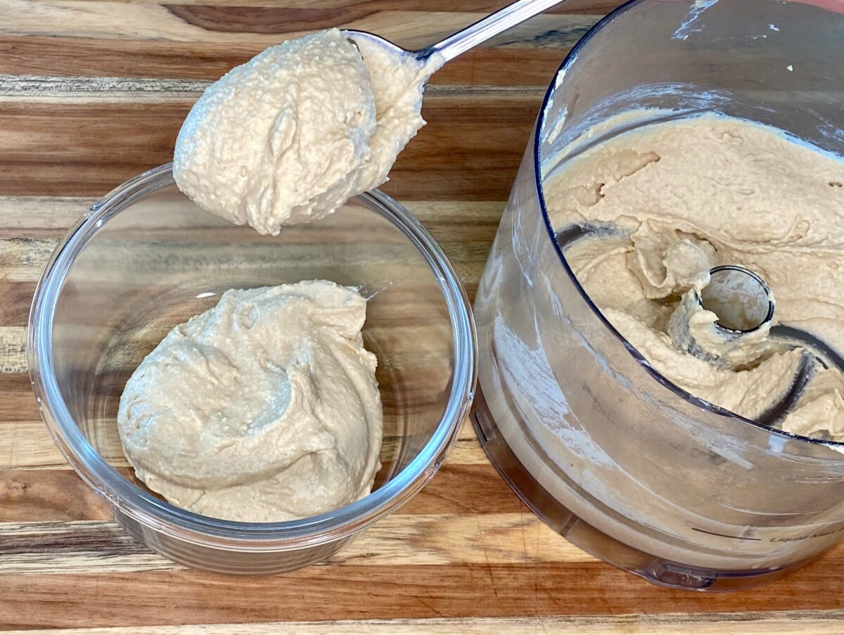 Transferring the hummus from the food processor into a bowl for serving and storage.