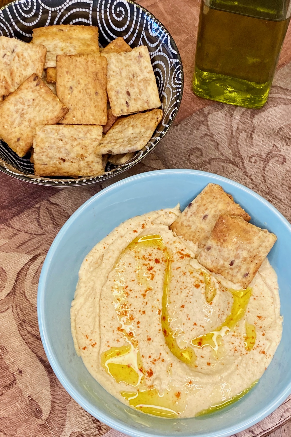 This hummus version skips the harissa topping and is simply served with a drizzle of extra virgin olive oil and a sprinkling of sweet paprika. Here, we're serving the hummus with pita crackers.