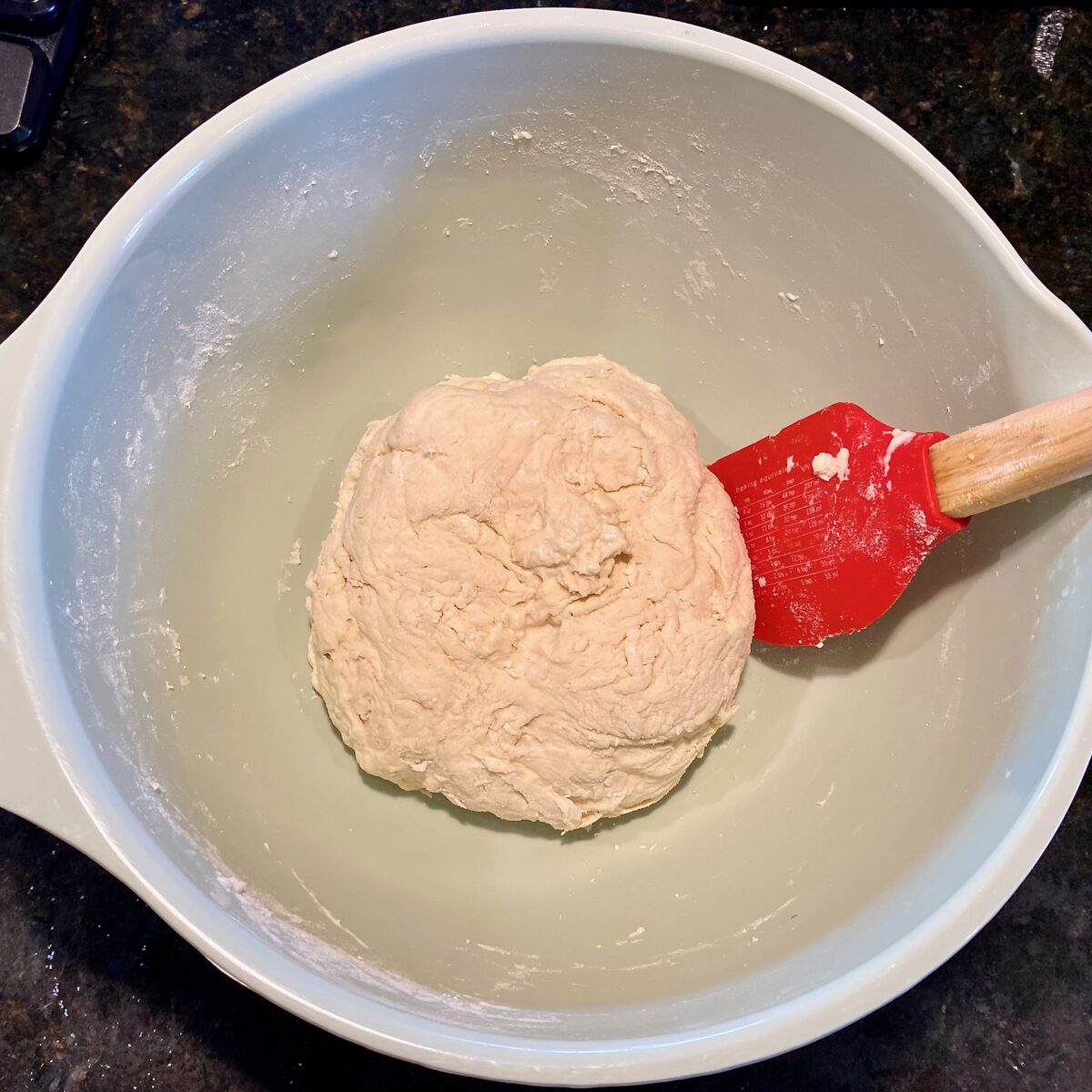 Using a silicone spatula to form a shaggy dough ball.