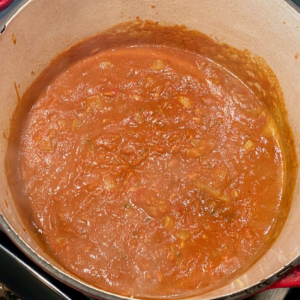 The chicken broth, water, tomato paste, sugar, and salt has now been added to the Dutch oven and whisked thoroughly to remove any lumps of tomato paste.