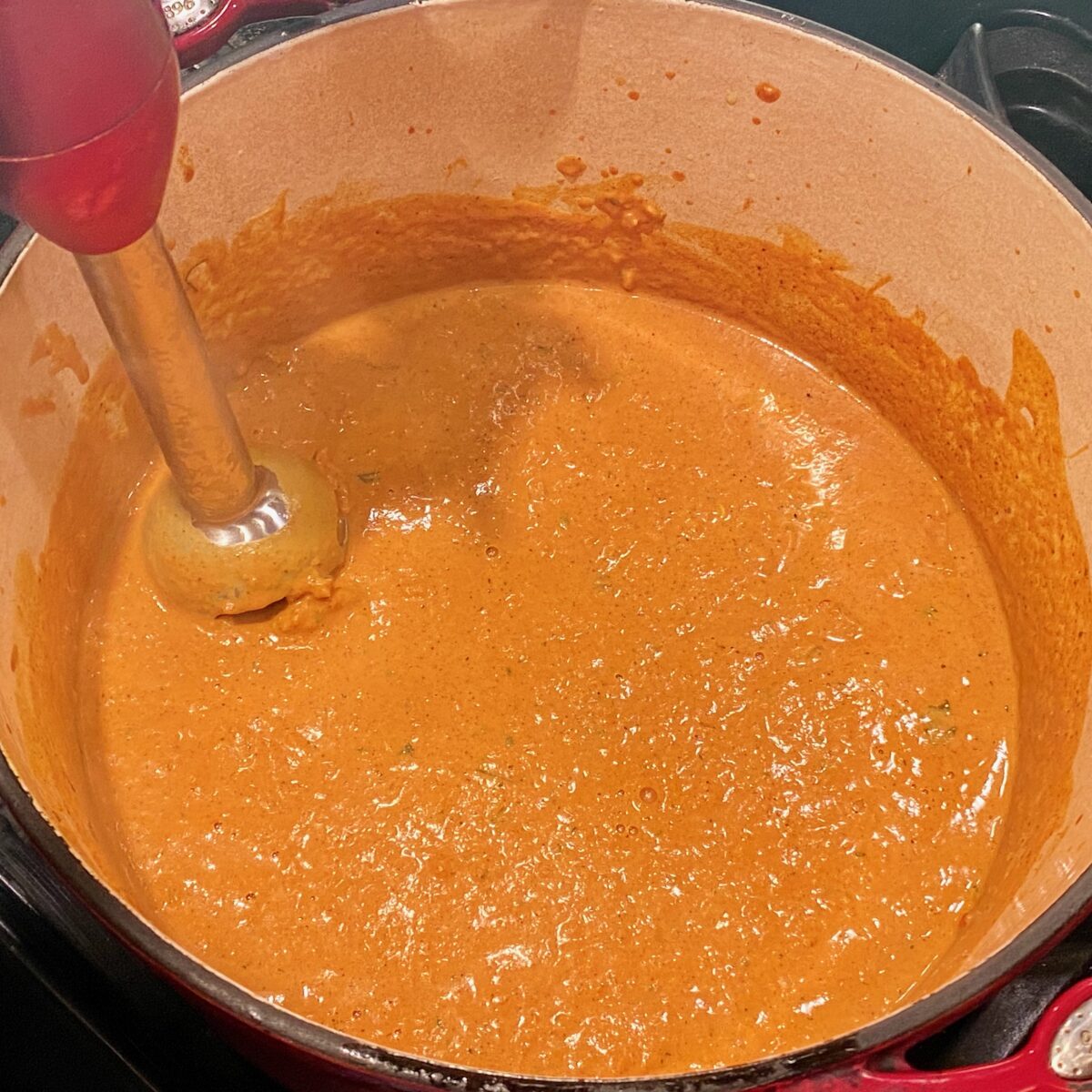 Pureeing the butter chicken sauce with an immersion blender.