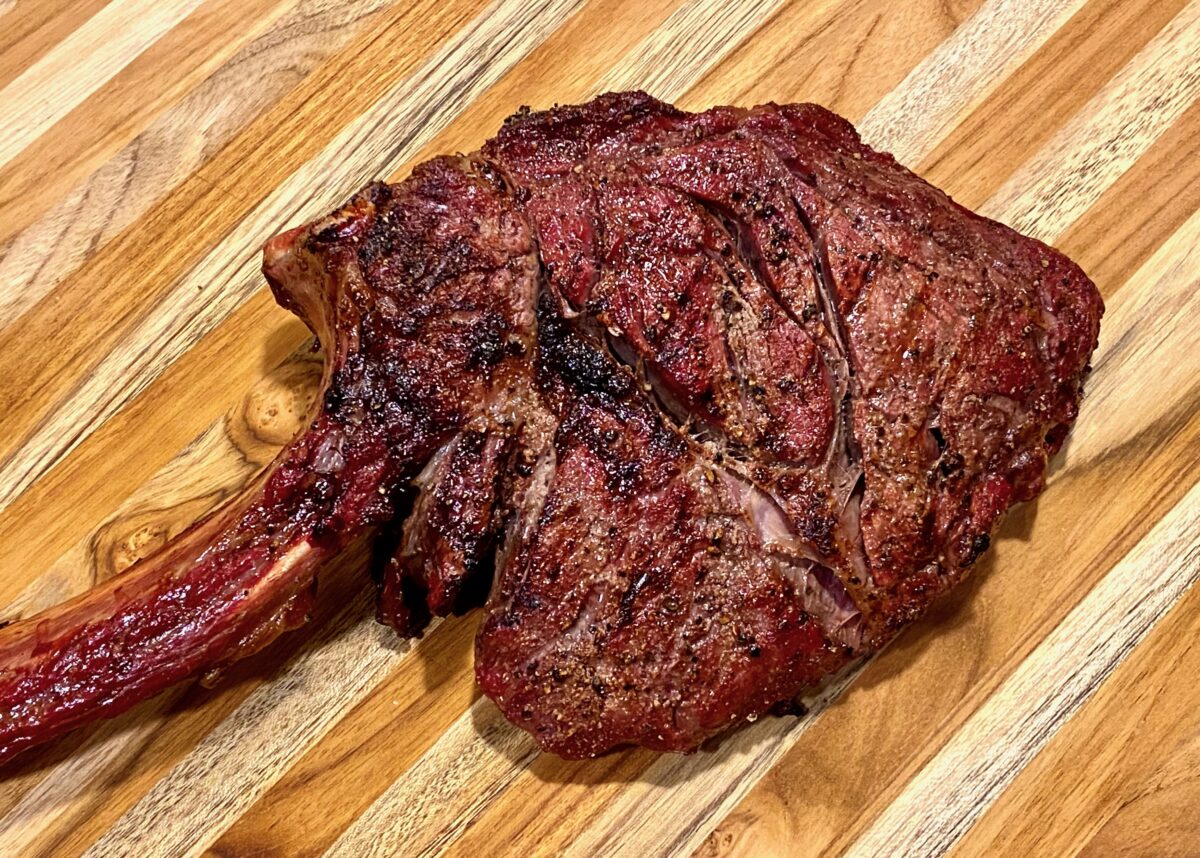 cooked Tomahawk steak resting on wood cutting board.