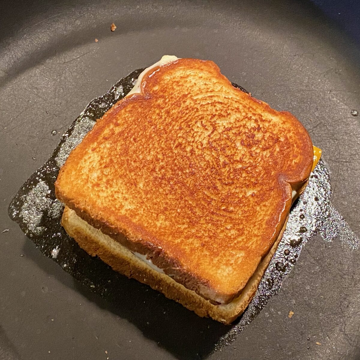 A grilled cheese sandwich made with Texas toast, with one side perfectly brown and crisp. The other side is browning up in melted butter.