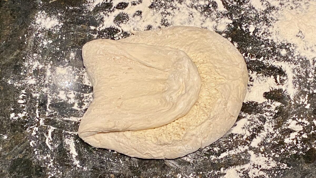 One side of the dough has been stretched out and folded back over the dough.