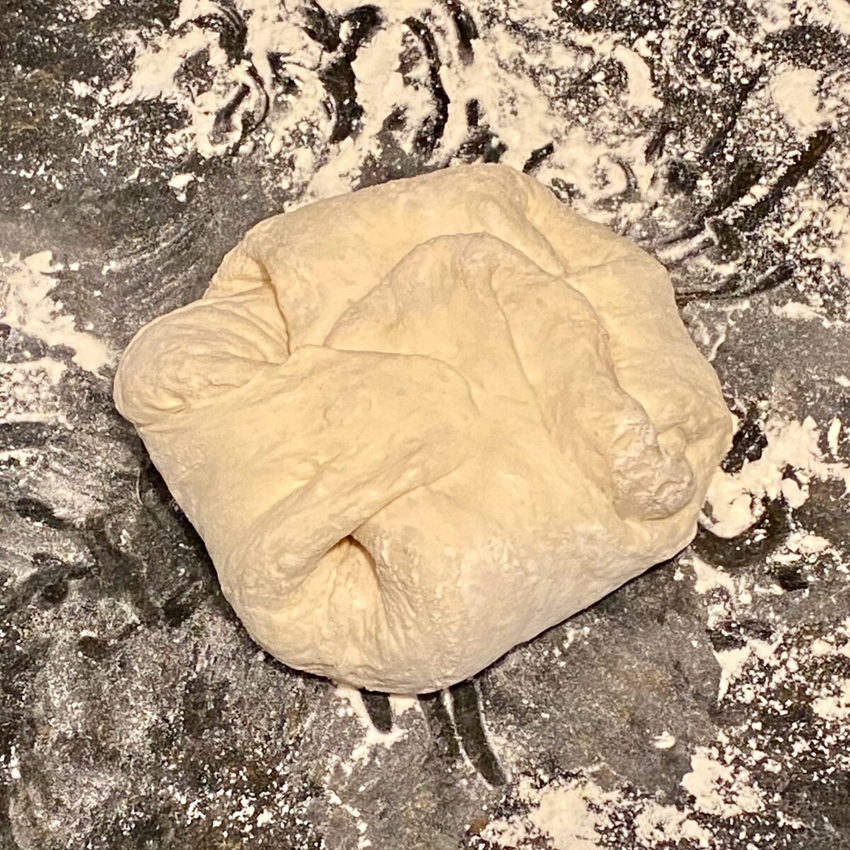 Now, each corner of the square-shaped dough has been stretched out and folded back over the dough.