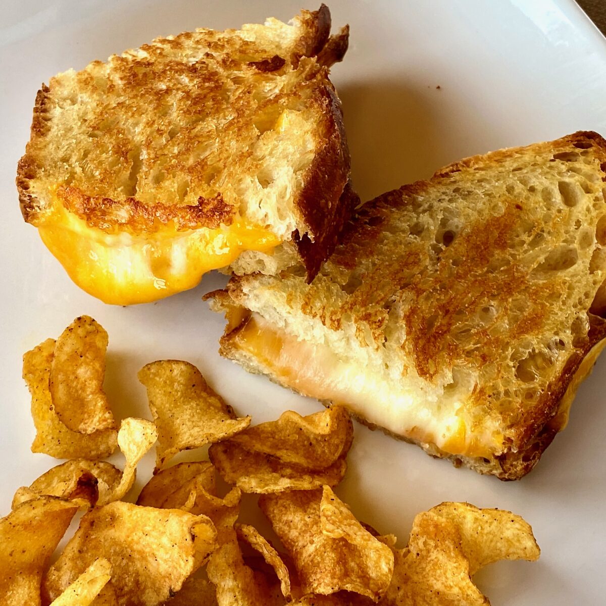 A perfectly melty, brown, and crisp grilled cheese on a plate with kettle chips.