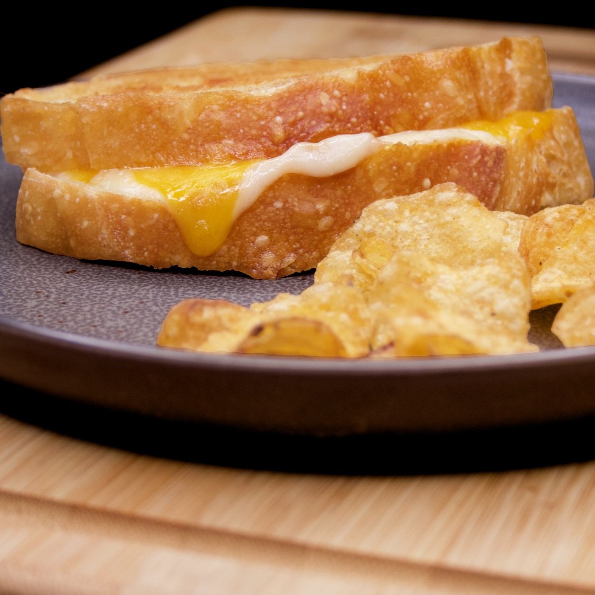 A perfectly melty grilled cheese sandwich on a plate with kettle chips.