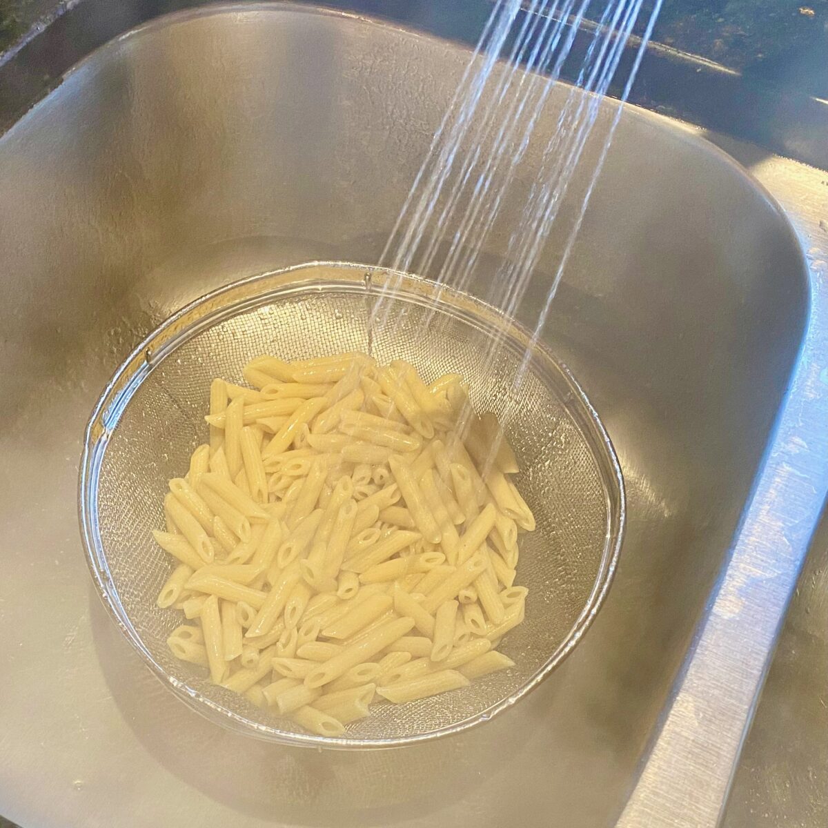 Draining the pasta and rinsing in cold water.