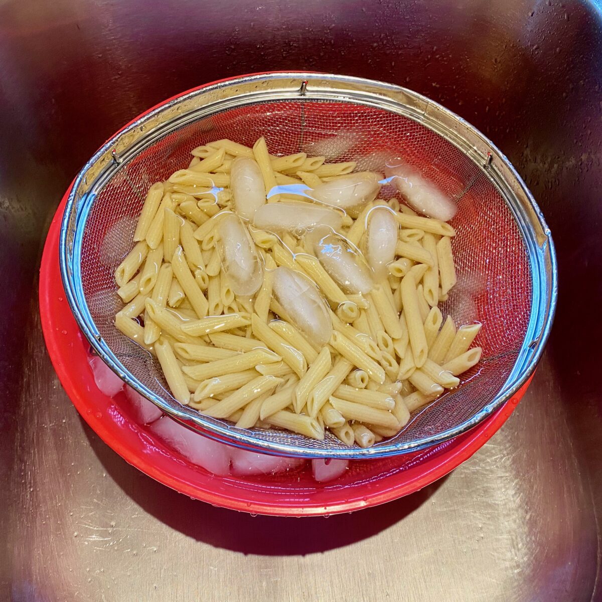 The colander of pasta cooling in a bowl of ice water.
