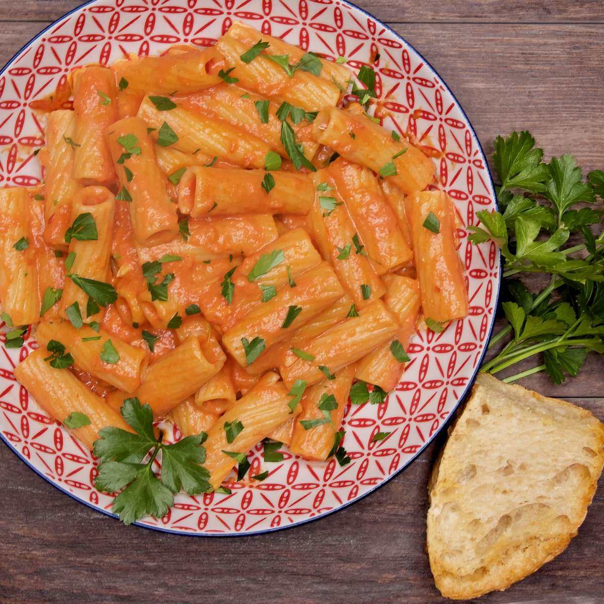 A serving of pasta alla vodka, sprinkled with chopped parsley and served with a slice of homemade rustic bread.