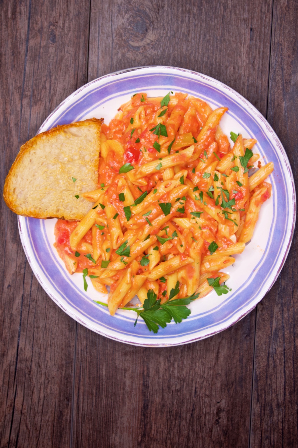 A serving of pasta alla vodka with a sprinkling of chopped parsley and a slice of rustic bread.