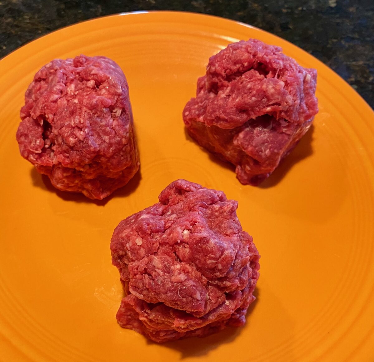 Three loosely formed balls of ground beef, ready to be placed onto a hot cast-iron griddle for making smash burgers.