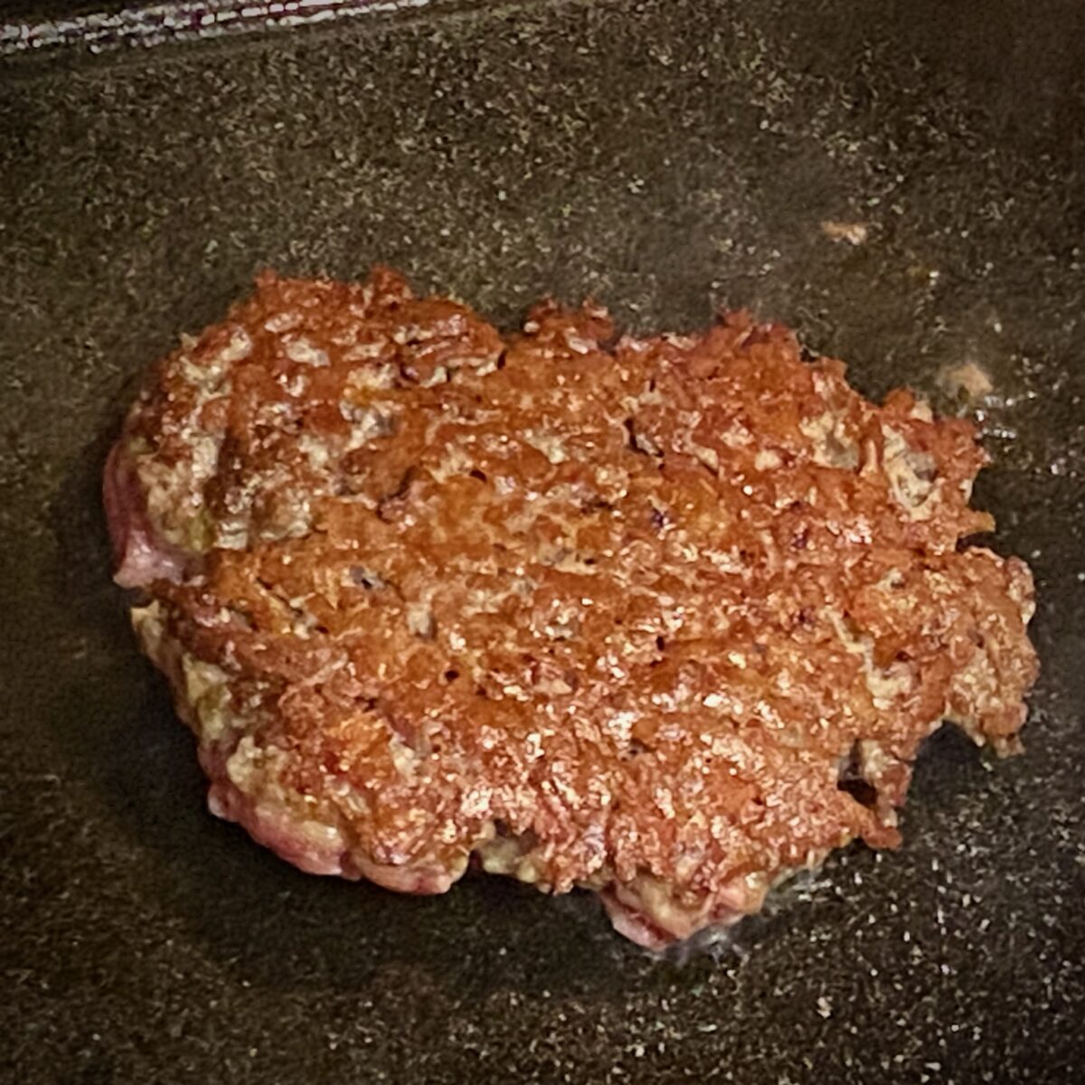 A flipped smash burger patty with a perfect, deep brown sear on one side.