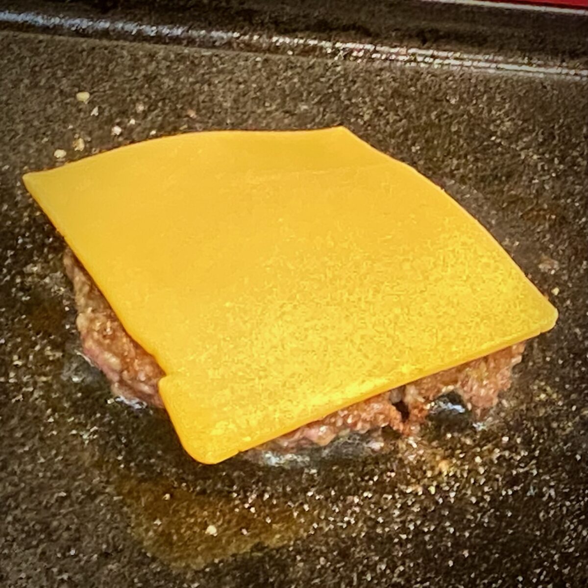 A slice of American cheese on top of a smash burger patty.