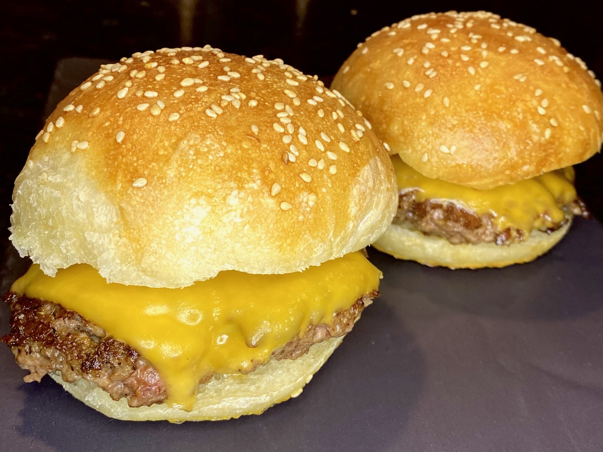 Two assembled smash burgers on home-baked sesame seed buns, ready to be devoured.
